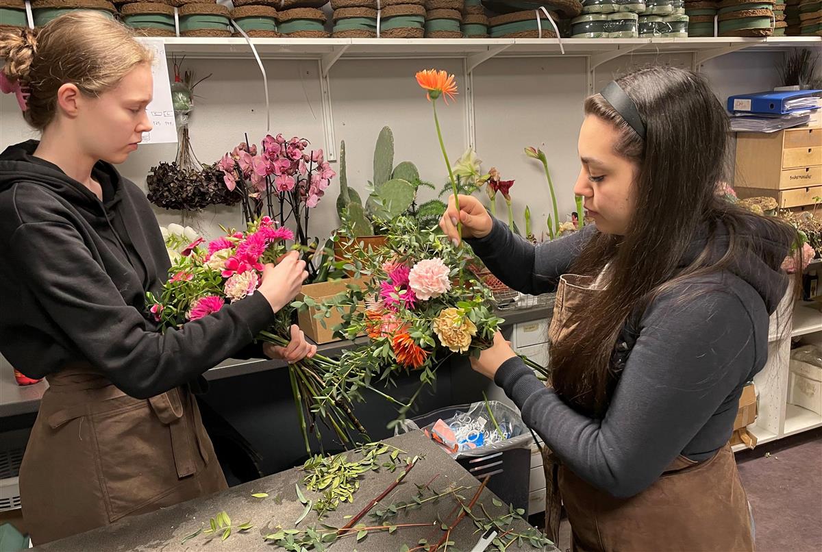 To unge kvinner setter sammen blomsterbuketter. - Klikk for stort bilde